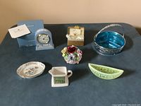 Photo of all seven pieces including Wedgewood clock in box, Wade dish and creamer, blue pickle tray, floral dish, green depression glass piece, and glass pineapple.