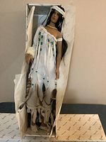 Porcelain doll inside original box, showing front view with detailed bead and feather decorations on white dress.
