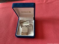 Birks vintage keychain inside blue velvet Birks box on red cloth background.