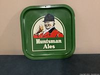 View of the front of the metal tray showing green background, huntsman figure and Huntsman Ales text