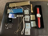 Full lot overview showing all watches, necklaces, earrings, and rings arranged on a black surface with most jewelry still on original cards and packaging.