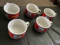 Five ceramic soup bowls on black surface showing Primo and Premium Plus red band designs with handles.