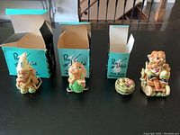 Four PenDelfin bunny figurines with their three open teal colored original boxes displayed in front of them