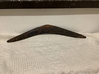 Wooden boomerang showing full curved shape and dark stain, laying flat on a white cloth.