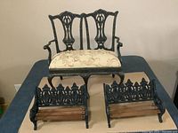 Miniature cast iron sofa with cream floral upholstery and two cast iron benches with wooden slats arranged on a flat surface.