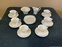 Full set arrangement showing cups on saucers, dessert plates stacked, cream pitcher and sugar bowl on black surface