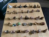 Photo showing 34 ceramic animal figurines arranged in rows on a wooden surface. Various species from birds to mammals and aquatic life visible.