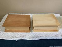 Two rectangular pine memory boxes with flat tops, one darker stained and one natural light pine, with closed lids placed on a lace cloth.