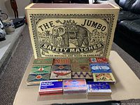 Large Jumbo Safety Matches box with black elephant illustration and 14 assorted smaller vintage matchboxes arranged in front, featuring various colorful brand labels.