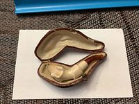 Miniature pipe placed inside the open brown leather case showing the light beige lining.