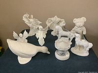 View of nine white ceramic pieces arranged including duck, carousel figures, angels, bear, and others