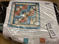 Photo showing quilt kit package with pattern and partial fabric information visible under plastic wrap.
