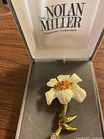Flower brooch with cream petals, orange stones in center, gold-tone stem inside Nolan Miller box