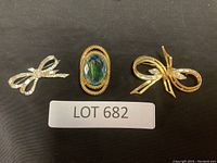 Three brooches displayed together on black background, showcasing different styles and materials.