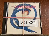 Top view of the CD case of the Quarterflash album 'Harden My Heart...' with lot label and rubber band.