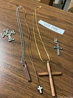 Photo showing the collection of five cross pendants with three attached to chains and two standalone crosses on a wooden surface.
