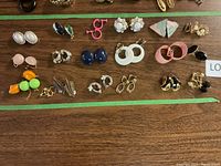 Photo showing the full assortment of 19 pairs of vintage clip-on earrings on a wooden surface.