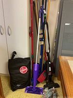 Photo of floor cleaning tools including Hoover vacuum bag, purple spray mop, Bissell handheld vacuum, and long-handled cleaning tools.