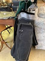 Black golf bag filled with golf clubs standing next to a sofa indoors.