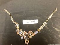 Full view of the multi-colored rhinestone statement necklace laid out on a black background, showing the gold-tone chain and decorative pendant area with various shaped stones.