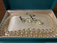 Full view of necklace and matching screw-back earrings displayed inside a teal jewelry box on a satin-like white cushion.