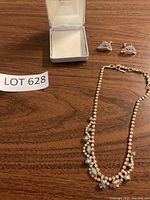 Photo of aurora borealis rhinestone necklace and matching clip-on earrings displayed on wood surface with jewelry box.