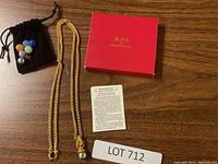 Photo showing gold tone chain necklace, red KJL box, black velvet pouch with marbles, and information card.