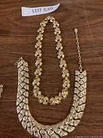 Two gold tone necklaces placed side by side on wooden surface, one with linked knot pattern and another with rhinestones and safety chain