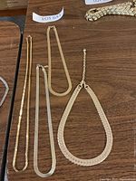 Four gold-tone necklaces displayed on a wooden surface showing different chain styles and lengths.