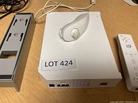 White Nintendo Wii console showing front and top with attached Nunchuk controller on top, and power/data ports visible on front.