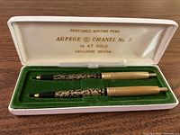 Two ARPEGE CHANEL No. 5 perfumed writing pens in original white case with green velvet holder and cream satin lid lining stamped with branding and 14kt gold mark.