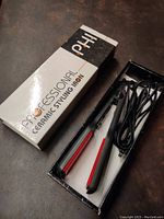 Ceramic styling iron in original box showing the styling iron with black body and red ceramic plates, power cord coiled beside it.