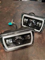 Pair of 4x6 rectangular LED fog projector lights with halo ring on a table, front-facing at an angle showing wiring and lens details.