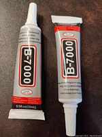 Two tubes of B-7000 glue side by side on a brown surface showing front labels.