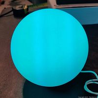 6-inch glowing ball illuminated with bright turquoise blue light, smooth surface, battery powered with visible power cable.