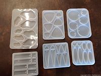 Top-down view of 6 white silicone molds with various shapes for jewelry making on a brown surface.