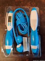 Top view of the digital counting skip rope in original plastic packaging showing blue and white handles and coiled blue rope.