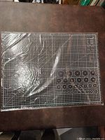 Clear view of the brand new double sided black cutting mat featuring grid lines and circular guides, covered in original packaging.