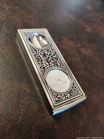Photo showing full metal rectangular cigar cutter with two circular openings and decorative engraving.