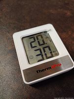 Front view of ThermoPro indoor humidity and temperature monitor showing temperature as 20°C and humidity 30%. LCD screen displays with a smiley face indicating comfort level.
