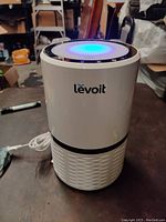 Front view of Levoit air purifier showing the white cylindrical unit with black vent band and visible power cable.