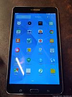 Front of Samsung Galaxy tablet powered on showing app icons on a bright screen.