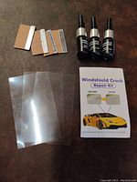 Photo showing 3 tubes of repair resin, adhesive strips, clear plastic sheets, and instruction manual for windshield crack repair.