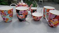 Tea set including 4 cups, teapot, creamer, and sugar bowl arranged on table showing floral designs and colors.