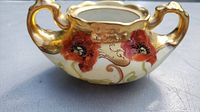 Front side view of the sugar bowl displaying pink poppy flowers and gold handles.