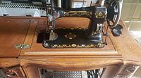 Side view of the black White Family Rotary sewing machine with floral gold and red detailing mounted in a wooden cabinet with carved wood details.
