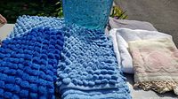 Blue plastic garbage can with three different blue bathmats and three towels (white and pink).