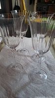 Four clear crystal stemware glasses arranged in a group on white cloth with vertical cut pattern on the bowls.