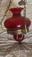 Full view of the ruby red glass hanging parlor lamp showing the wide flared top, ornate metal sections, and chain for hanging.