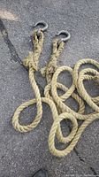 Photo showing the length of natural fiber rope with two large metal hooks at the ends, coiled roughly on asphalt surface.